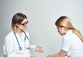 dokter zit Aan een stoel en een vrouw geduldig binnenshuis Aan een licht achtergrond foto