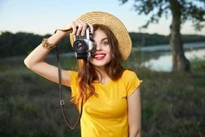 vrouw Holding camera looks in de camera lens rood lippen hoed natuur foto