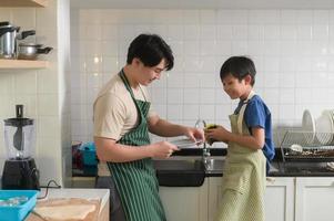 gelukkig glimlachen jong Aziatisch vader en zoon het wassen gerechten in keuken Bij huis foto