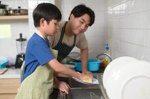 gelukkig glimlachen jong Aziatisch vader en zoon het wassen gerechten in keuken Bij huis foto