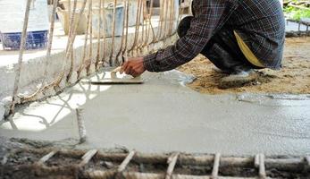 werknemer met behulp van houten troffel voor het egaliseren van de betonnen vloer foto