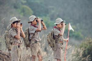 Amerikaans jongen verkenners in uniform zitten kijker in een groen veld- Aan een berg wandeltocht gaan naar zomer kamp. foto