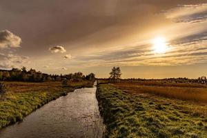 versmallen rivier- vloeiende door weiden tegen de backdrop van wolken gedurende zonsondergang foto