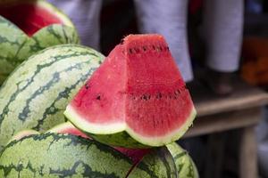 rijp rood een plak van watermeloen met veel watermeloenen zijn verkocht in de markt in de zomer warmte foto