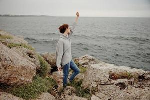 vrouw in een grijs trui staat Aan een rotsachtig kust natuur ongewijzigd foto