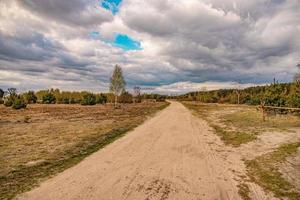 voorjaar landschap met een aarde weg, velden, bomen en lucht met wolken in Polen foto