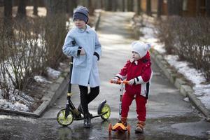 kinderen met scooters. de ouder zus en jonger broer zijn spelen Aan de straat. foto