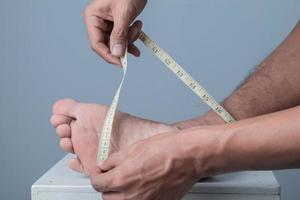 detailopname van een Mens meten zijn voet grootte met een meten plakband tegen een licht blauw achtergrond foto
