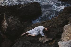 vrouw in een afgelegen plek Aan een wild rotsachtig kust in een wit jurk ongewijzigd foto