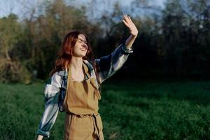 portret van een mooi jong vrouw met rood haar- in natuur in een park in de zomer, op zoek Bij de zonsondergang tegen een achtergrond van groen gras en bomen foto