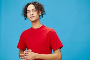 aantrekkelijk schattig jong gekruld gebruind Kaukasisch vent in eenvoudig rood t-shirt looks Bij camera poseren geïsoleerd Aan over- blauw achtergrond. levensstijl en emoties concept. mooi zo aanbod met kopiëren ruimte voor advertentie foto