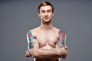 sexy bodybuilder met naakt torso gemaakt van spier tatoeages grijs achtergrond gekruiste armen Aan borst foto