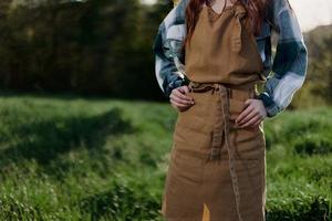 detailopname van een vrouw in een tuinman werk schort tegen de groente, vers zomer gras buitenshuis tonen haar handen foto