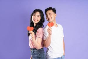 beeld van Aziatisch paar Holding een hart sticker, geïsoleerd Aan Purper achtergrond foto