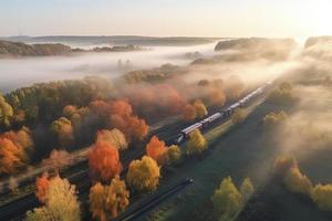 antenne visie van vracht trein in mooi Woud in mist Bij zonsopkomst in herfst. kleurrijk landschap met spoorweg foto