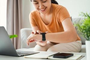 jong vrouw op zoek en gebruik makend van een smartwatch, vrouw zittend Aan de sofa controle haar smartwatch. foto