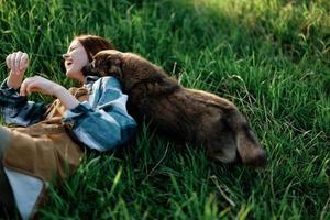 een vrouw leugens Aan de gras glimlachen en knuffelen haar hond in natuur in een park in de zomer zonsondergang. de concept van Gezondheid en liefde voor dieren, behandeling tegen teken foto