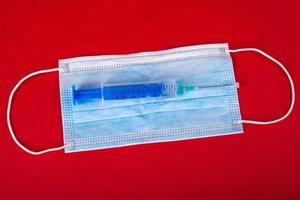 blauw medisch beschermend masker en spuit met een vaccin op een rode achtergrond foto