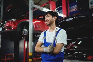 portret van glimlachen Aziatisch mannetje klusjesman Holding met gekruiste benen moersleutel Bij garage professioneel reparatie en onderhoud. auto inspectie onderhoud foto