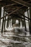 golven onder een houten visvangst pier Bij de strand foto