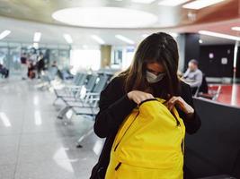 een vrouw zit Bij de luchthaven en looks in een geel rugzak passagier foto