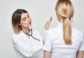 dokter vrouw in een medisch japon met een stethoscoop communiceert met een geduldig terug visie foto
