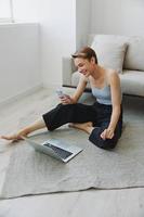 freelance vrouw met laptop en telefoon werken van huis zittend Aan de verdieping in haar huis kleren met een kort kapsel, vrij kopiëren ruimte foto