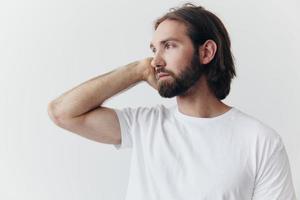 portret van een Mens met een zwart dik baard en lang haar- in een wit t-shirt Aan een wit geïsoleerd achtergrond emotie van droefheid en verlangen foto