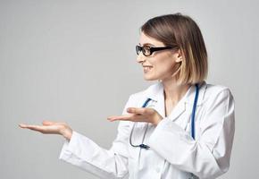 vrouw verpleegster in een medisch japon gebaren met haar handen Aan een licht achtergrond foto