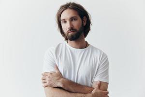 portret van een Mens met een zwart dik baard en lang haar- in een wit t-shirt Aan een wit geïsoleerd achtergrond levensstijl zonder pathos elke dag beeld foto