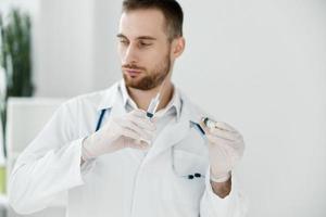 een professioneel dokter in een medisch japon is aanhankelijk en in beschermend handschoenen houdt een ampul met een vaccin foto