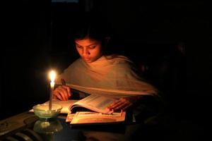 een jong meisje aan het studeren Bij huis met kaarslicht na elektriciteit laden vergieten Bij Dhaka stad. foto