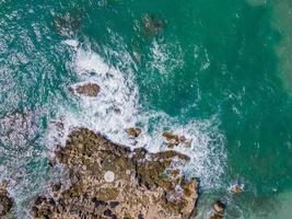 antenne visie van zee crashen golven wit schuimend golven Aan kust rotsen top visie foto