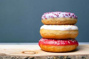 drie geassorteerde geglazuurde donuts van verschillende kleuren op een houten plank op een grijze achtergrond foto