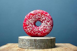 donut met rood glazuur en wit poeder op een houten standaard op een grijze achtergrond foto
