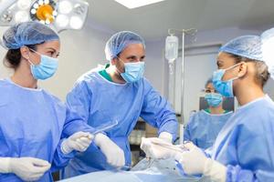 chirurgen mannen en Dames in een team gedurende een operatie over- de in werking tafel, artsen in modern uitrusting uitvoeren een oncologisch operatie foto