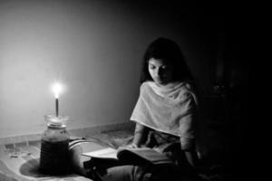 een jong meisje aan het studeren Bij huis met kaarslicht na elektriciteit laden vergieten Bij Dhaka stad. foto