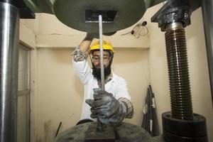 Bangladesh mei 20, 2015 een fabriek laboratorium operator gebruik makend van staal hengel sterkte testen machine foto