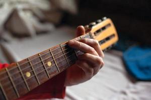 man speelt een melodie op een akoestische gitaar terwijl hij zijn hand op de toets houdt foto