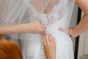 de bruidsmeisjes helpen de bruid zetten Aan haar bruiloft jurk. detailopname van handen foto