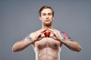 mannetje atleet met een appel in zijn handen en tatoeëren kubussen Aan zijn maag biceps druk op foto