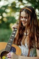 gelukkig hippie vrouw met een gitaar ontspannende in natuur zittend Aan een plaid glimlachen en genieten van de visie. levensstijl in harmonie met natuur en zelf foto