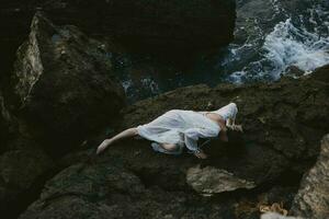 mooi jong vrouw in lang wit jurk nat haar- aan het liegen Aan een rotsachtig klif zomer vakantie concept foto