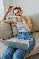 tiener- meisje freelancer met laptop zittend Aan bankstel Bij huis glimlachen in huis kleren en bril met kort kapsel, levensstijl met Nee filters, vrij kopiëren ruimte foto