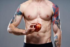 jong Mens met appel en gemotiveerd omhoog torso biceps Mens tatoeëren grijs achtergrond bijgesneden visie foto