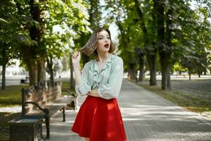 mooi blond in rood rok buitenshuis in de park groen bomen foto