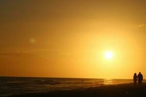 strand zonsondergang met sommige wolken mensen silhouet foto