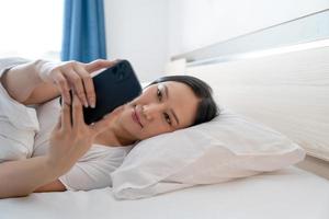 Aziatisch vrouw gebruik makend van smartphone Aan bed in slaapkamer mobiel verslaving concept. foto