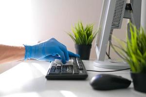 mannetje handen in rubber handschoenen veeg de toetsenbord van de computer. ontsmetting in de kantoor gedurende covid-19 foto