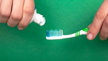 hand knijpt tandpasta op een tandenborstel op een groene achtergrond close-up